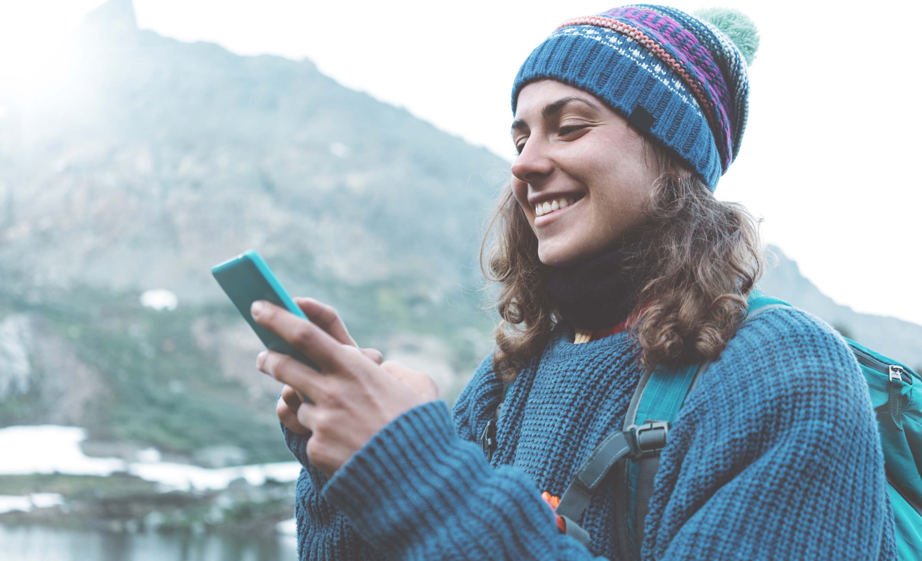 Young, white, woman smiling while using her mobile phone outside in cold weather.