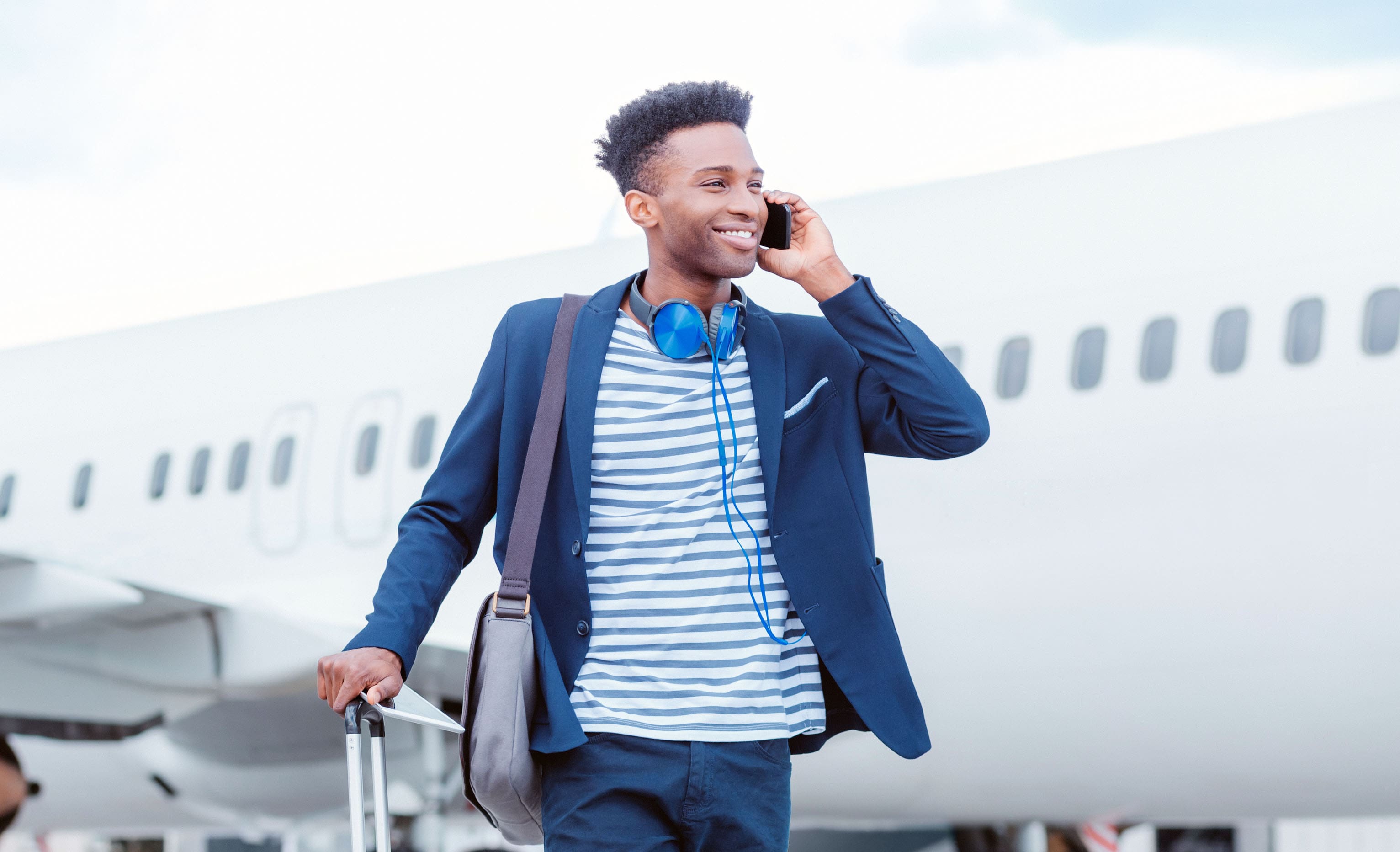 Young, black, man standing at airport talking on a cellphone