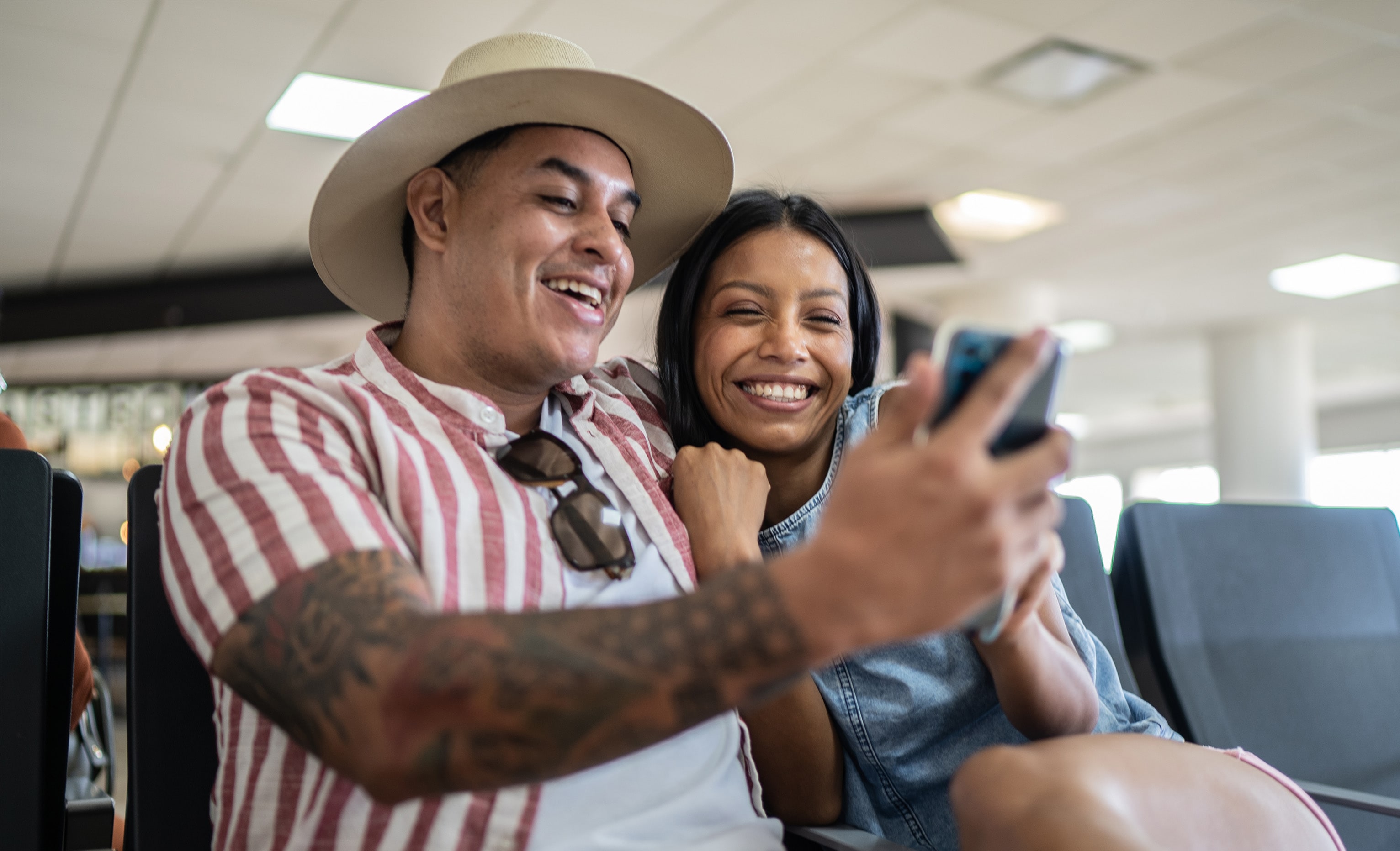 Latino couple smiling while looking at mobile phone in airport lobby